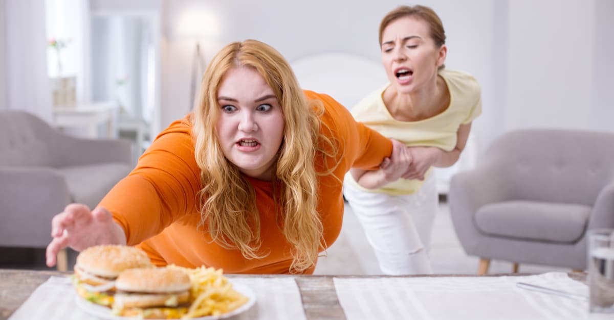 woman with a food addiction reaching for cheeseburgers and fries