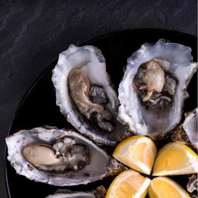 oysters served with lemon wedges on a black plate sitting on grey background