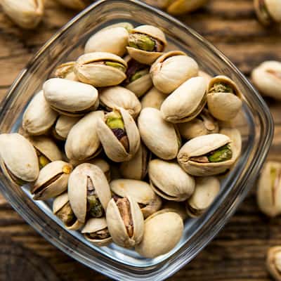 pistachios in a small bowl with scattered nuts on a wooden table