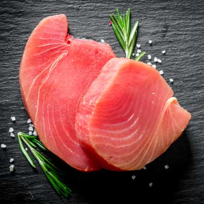 fresh raw tuna steak with rosemary on black slate background