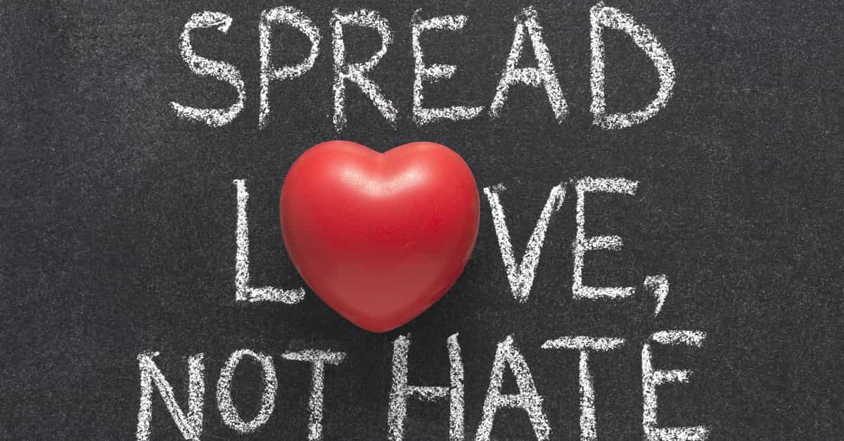 spread love, not hate phrase handwritten in white chalk on a blackboard with a red heart symbol instead of O in love