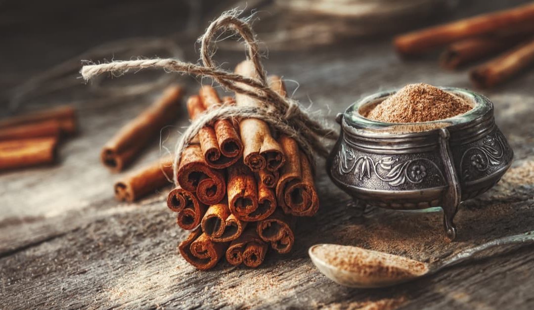 Ground cinnamon and cinnamon sticks, tied with jute rope on a rustic style wooden background