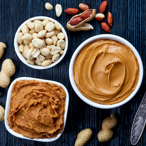 two bowls of peanut butter and peanuts on dark wooden background