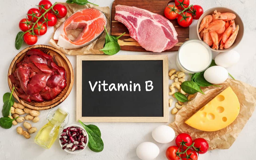 Assortment of high vitamin B sources on white background: milk, liver, olive oil, tomatoes, prawns, peanuts, beef, spinach, salmon, cashew, cheese, eggs, haricot.