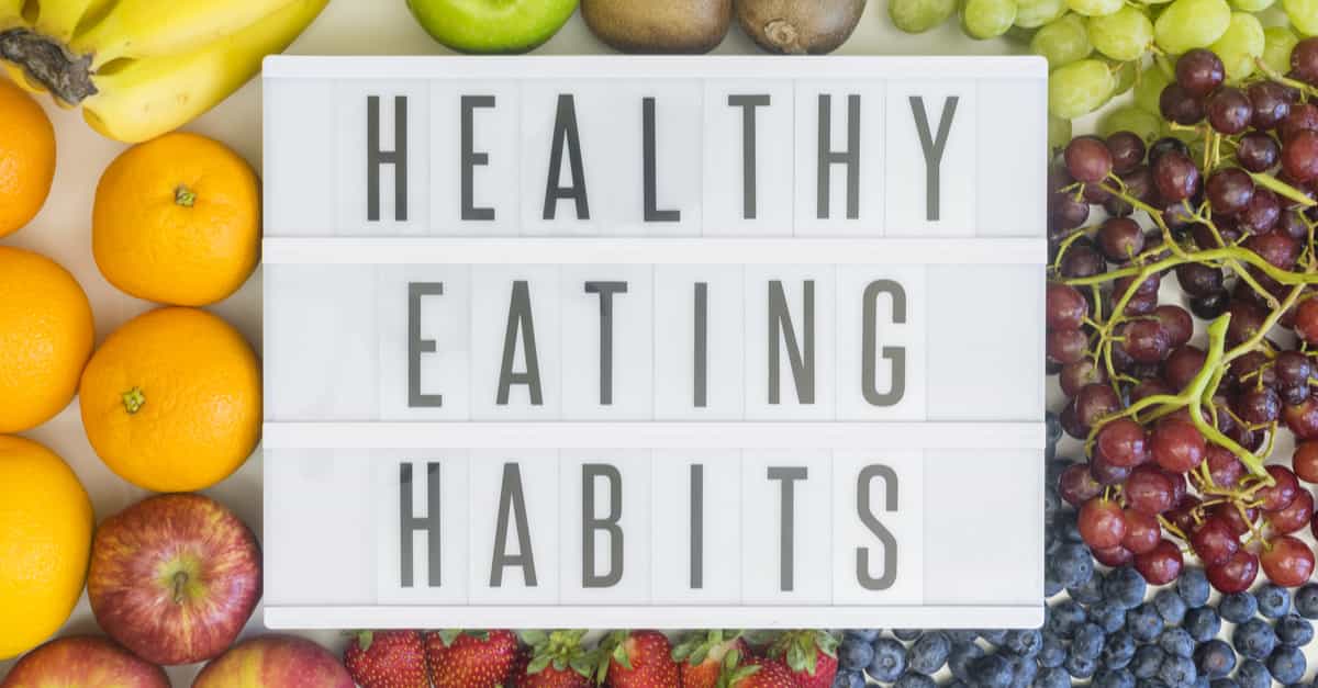 Healthy eating habits written on a light box with fruit in the background.