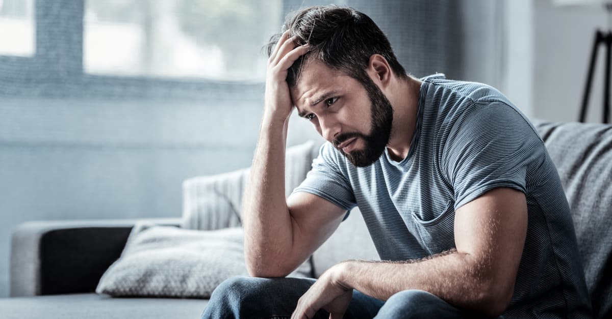 Unhappy man sitting on the sofa and holding his forehead looking depressed